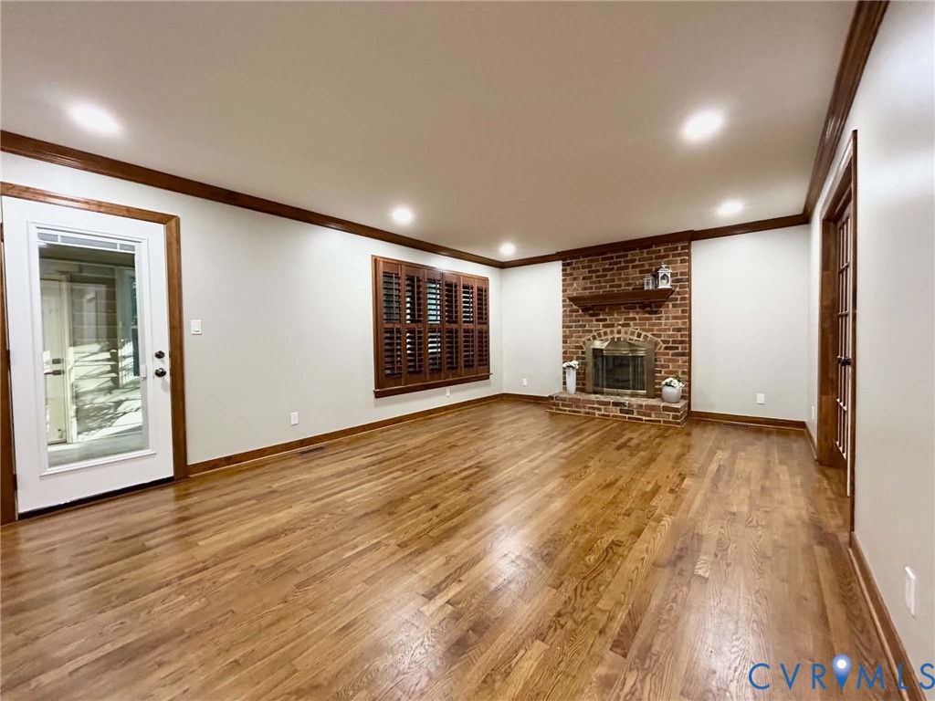 Interior space featuring wood-finish flooring, a brick fireplace with a wood mantel, crown molding, plantation shutters, and recessed lighting