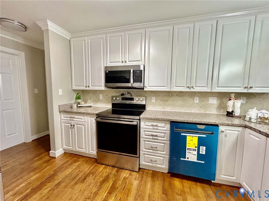 Kitchen featuring white shaker-style cabinetry, stone-finish countertops, stainless steel appliances, a diamond-pattern tile backsplash, and wood-finish flooring