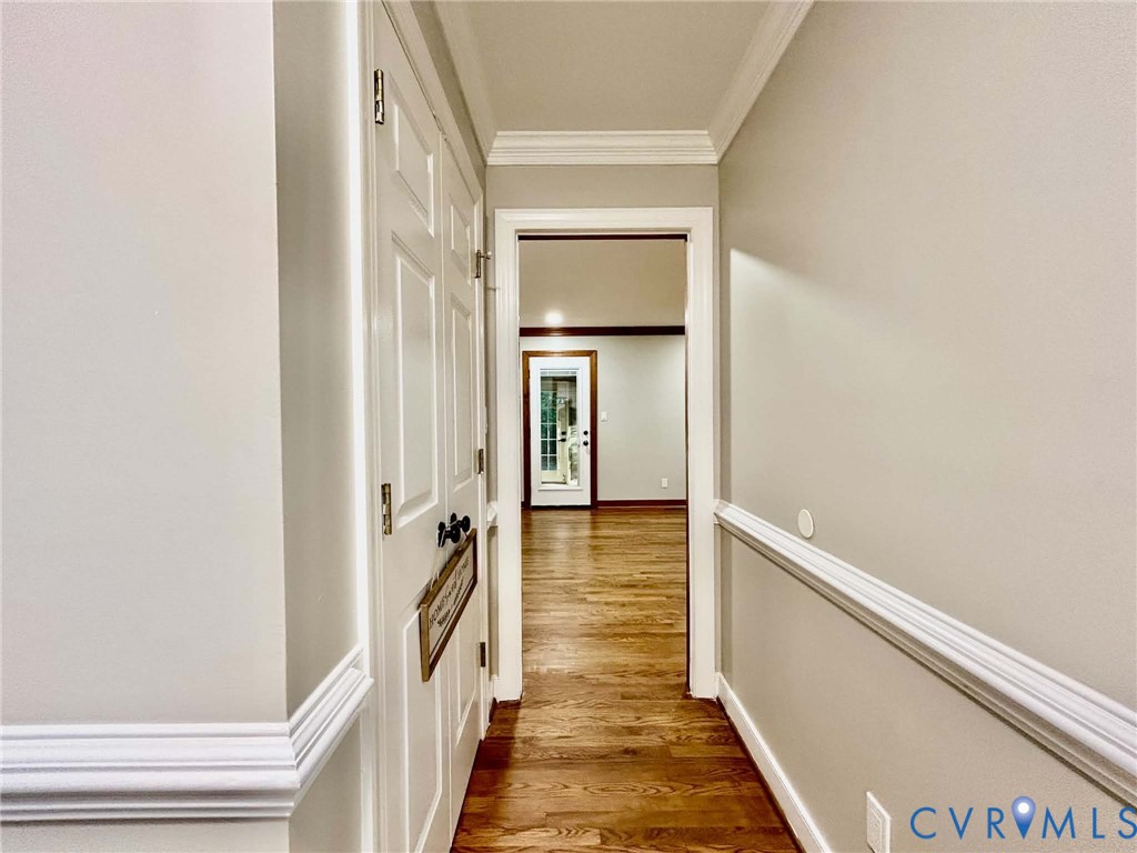 Interior hallway featuring wood-finish flooring, crown molding, chair rail trim, and a double-door closet