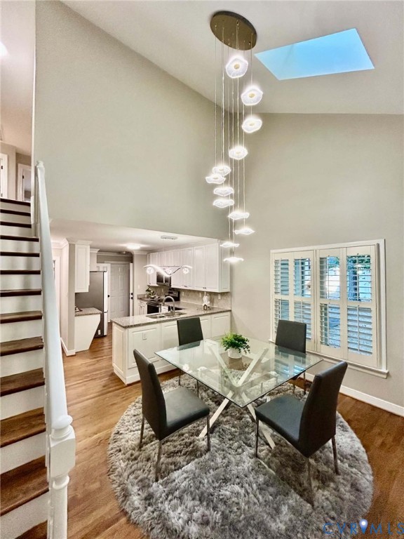 Vaulted ceilings featuring a multi-pendant light fixture and skylight, wood-finish flooring, staircase with white railing, and interior shutter window treatments