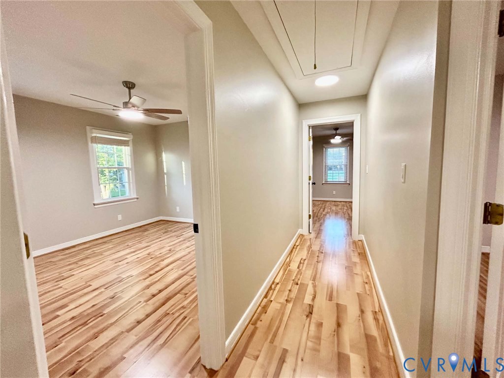 Hallway featuring wood-finish flooring, recessed ceiling lighting, and attic access, with entry points to rooms containing wood-finish flooring, multi-pane windows, and ceiling fans