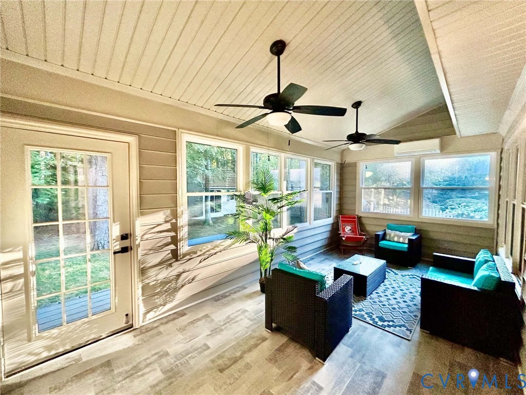 Enclosed porch featuring wood-finish flooring, beadboard ceiling, dual ceiling fans, wall-mounted climate control unit, and multiple windows with muntin detailing