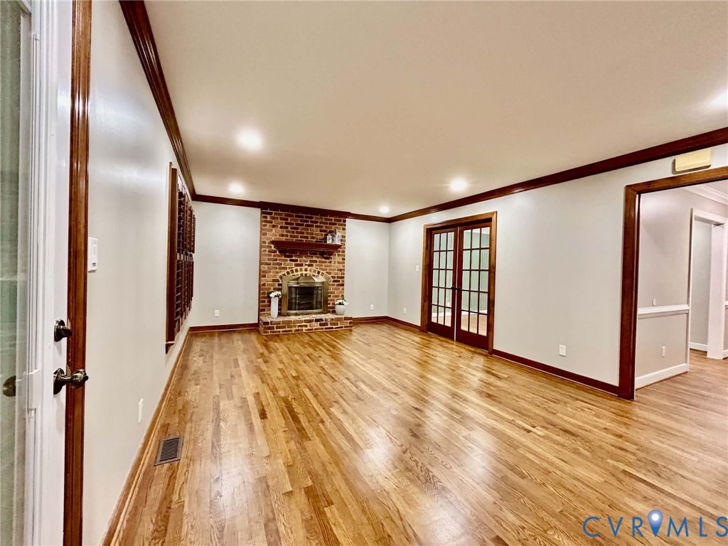 Wood-finish flooring, brick fireplace with a wood mantel, recessed lighting, and glass-paned French doors with stained wood trim