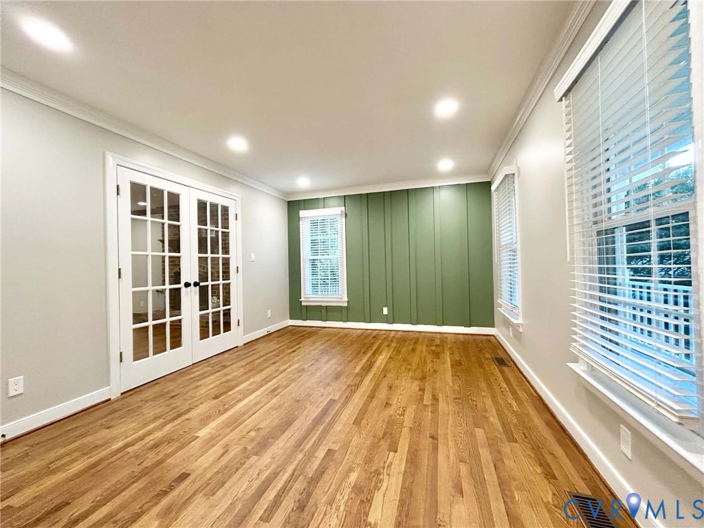 Wood-finish flooring, vertical board-and-batten accent wall, recessed lighting, and white-trimmed glass-paneled double doors