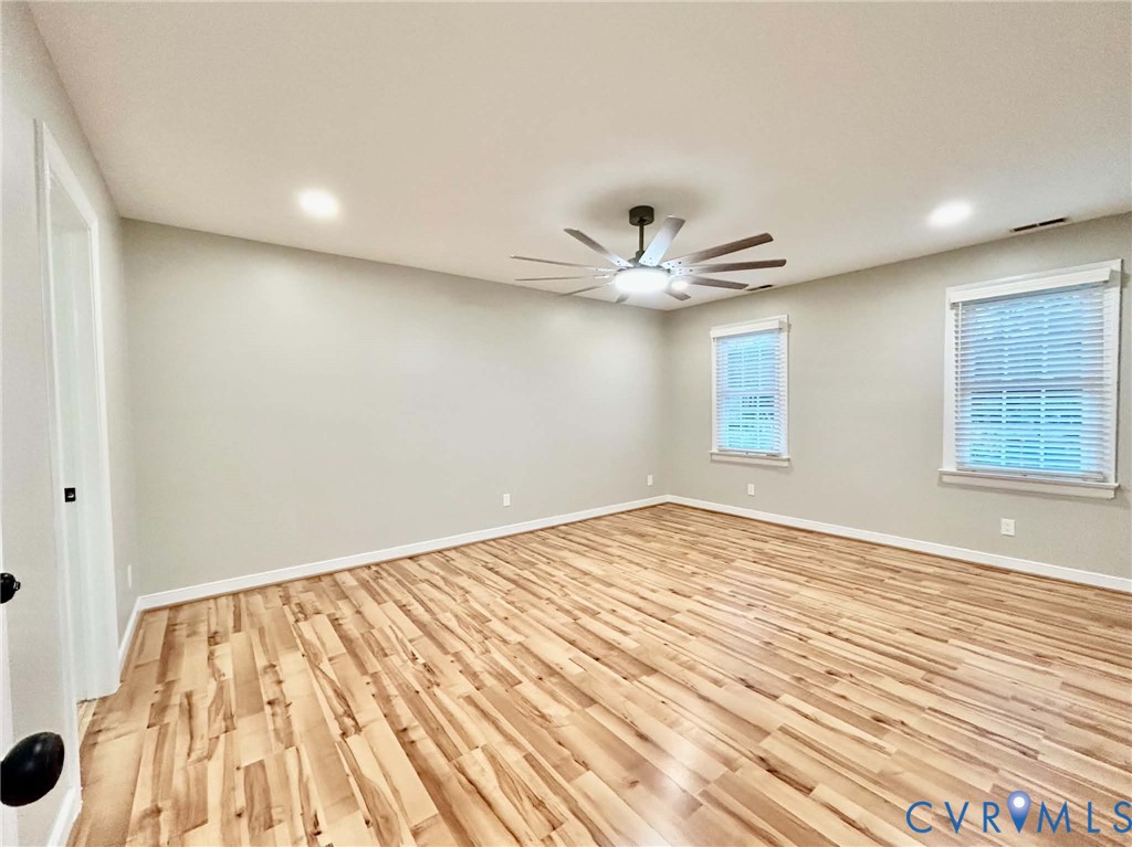 Neutral-toned interior featuring wood-finish flooring, recessed lighting, a multi-blade ceiling fan with integrated light fixture, and dual windows with window blinds