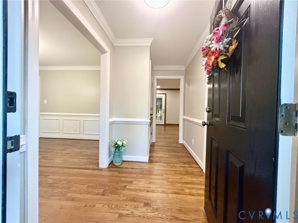 Entryway featuring wood-finish flooring, crisp crown molding, and wainscoting