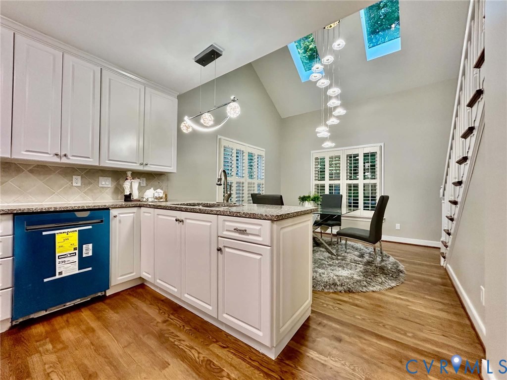 Kitchen featuring white cabinetry, stone-surface countertops, dual skylights, wood-finish flooring, and a multi-tiered decorative pendant light fixture
