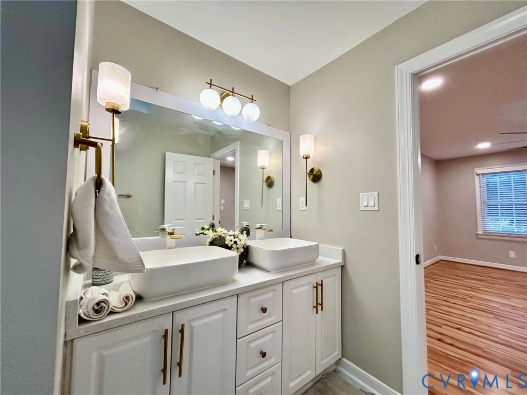 Dual rectangular vessel sinks atop a white vanity with brass hardware, illuminated by a tri-bulb vanity light and matching brass wall sconces, featuring a large wall-mounted mirror