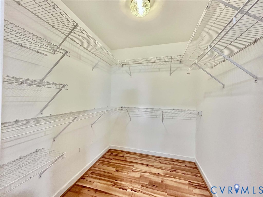 Walk-in storage space featuring wood-finish flooring, white walls, and multi-tier wire shelving with an overhead flush-mount light fixture