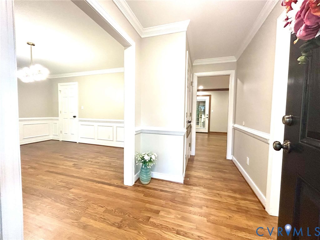 Entryway featuring wood-finish flooring, wainscoting, crown molding, a multi-light chandelier, and a solid-core entry door with metallic hardware