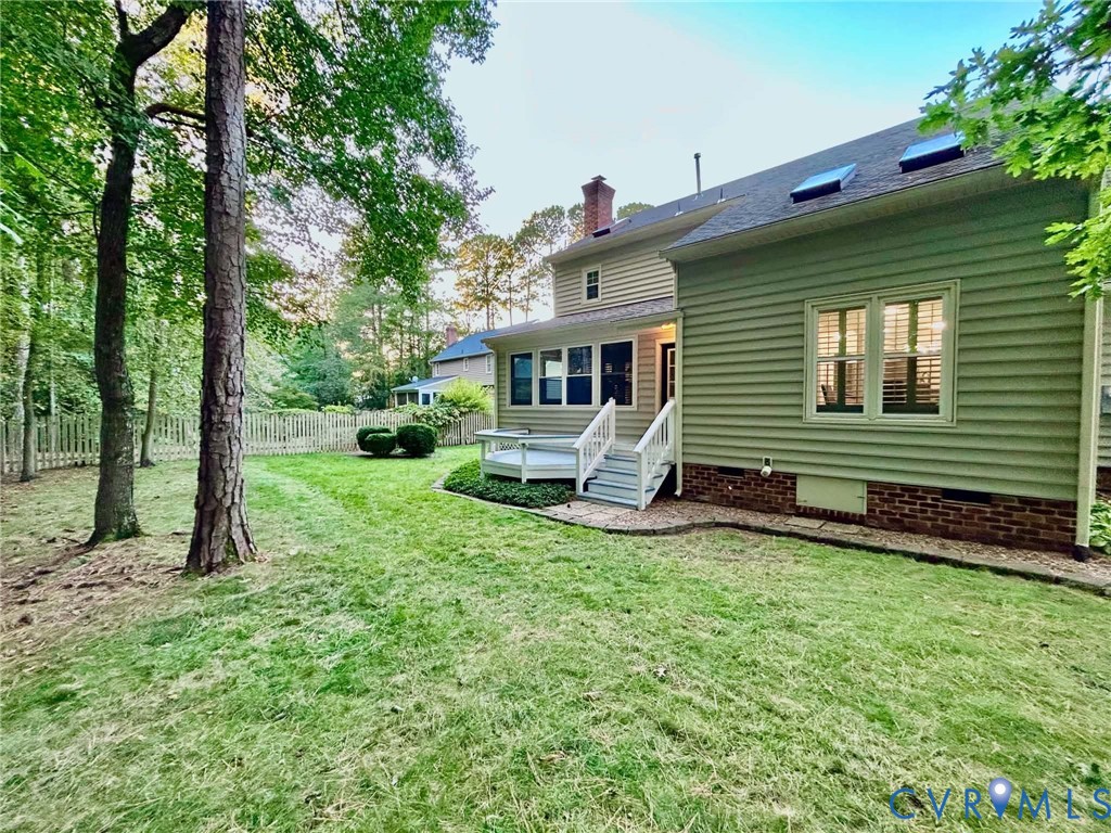 Exterior featuring lap siding, brick foundation, elevated wood deck with railing, skylights, and a fenced rear yard with mature trees
