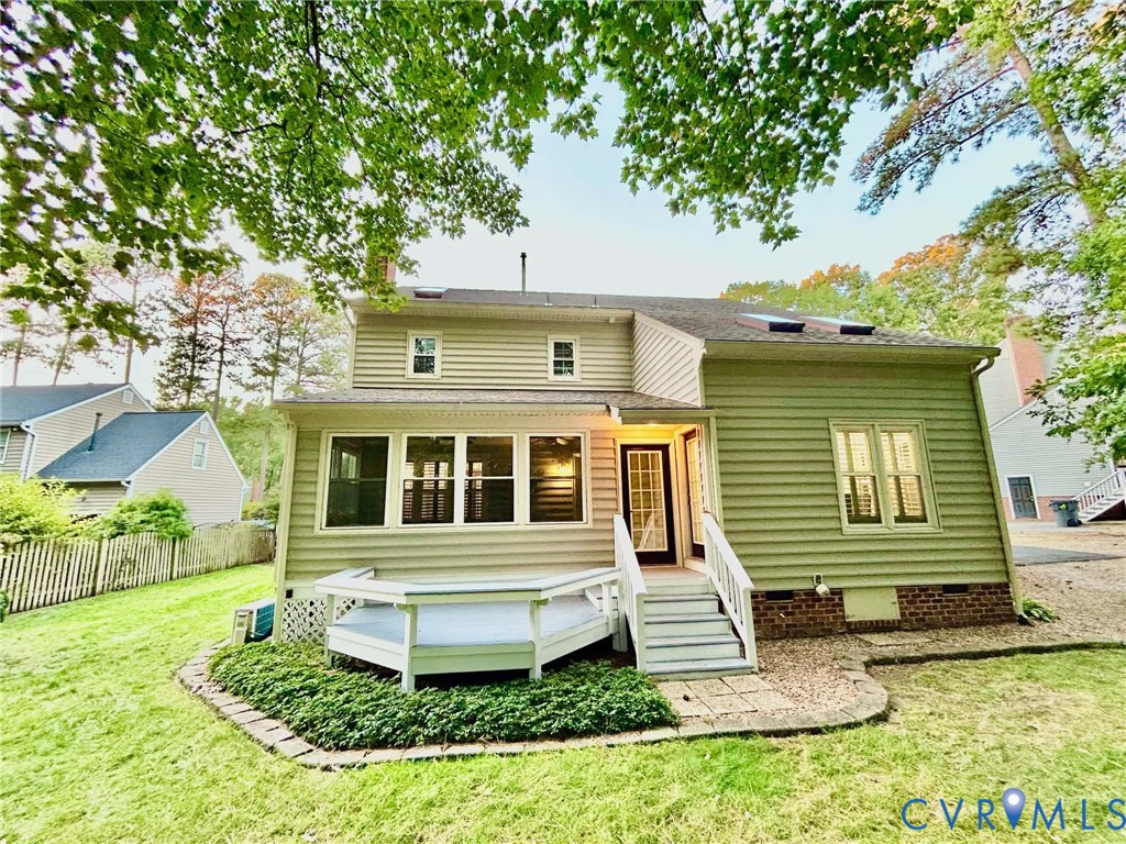 Rear exterior featuring light-colored horizontal siding, a raised white deck, brick foundation accents, roof-integrated skylights, and a stone-bordered garden bed