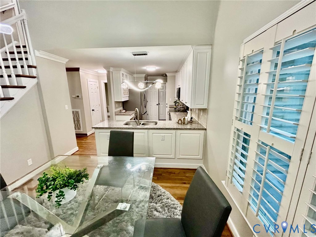 Kitchen featuring white shaker-style cabinetry, solid-surface countertops, wood-finish flooring, and plantation shutters