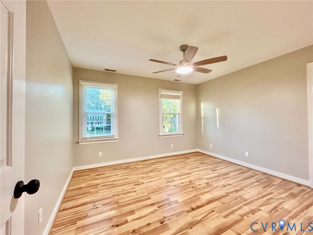 Room featuring wood-finish flooring, neutral wall paint, two double-hung windows with integrated blinds, and a central ceiling fan with an integrated light fixture