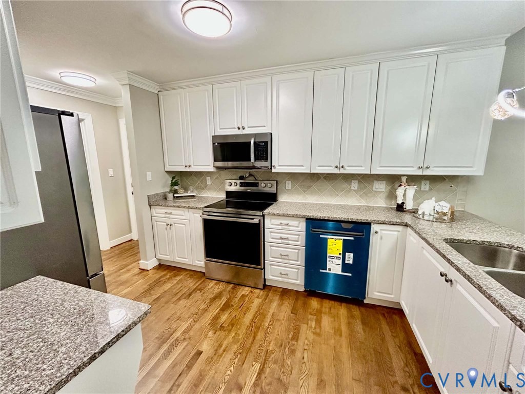 Kitchen featuring white shaker-style cabinetry, stone-finish countertops, tile backsplash, stainless steel appliances, and wood-finish flooring