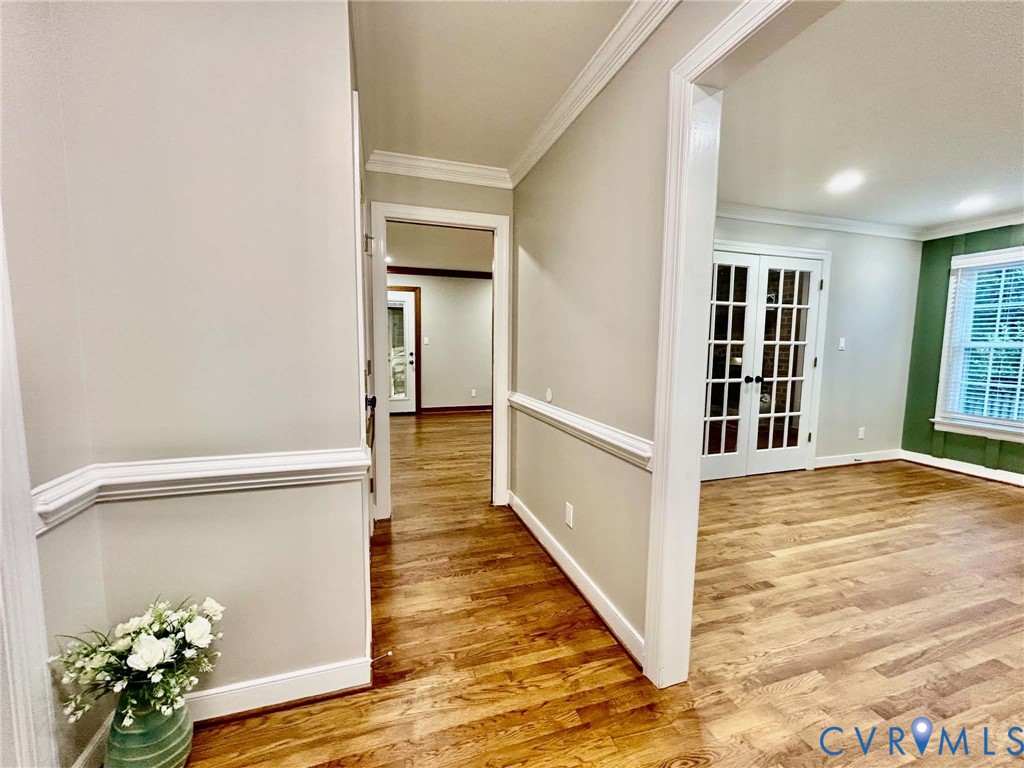 Interior featuring wood-finish flooring, crown molding, chair rail trim, and glass-paned French doors