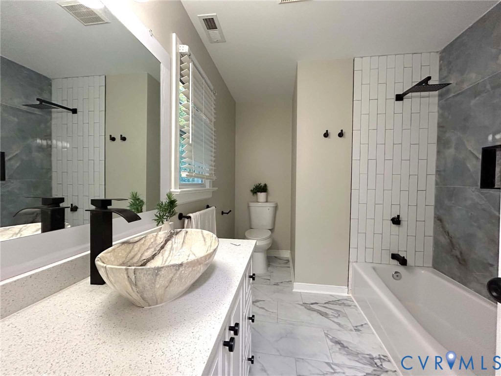 Bathroom featuring a vessel sink with a matte black faucet, light-toned countertop, vertical white subway tile tub surround, and patterned flooring