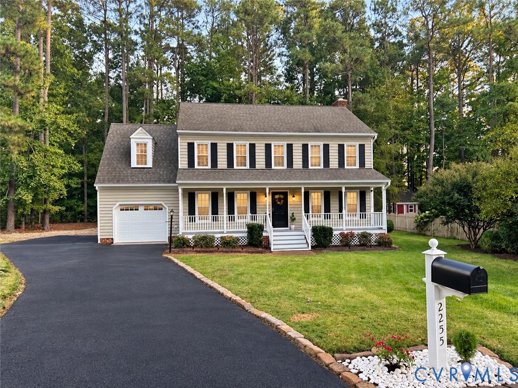 Two-story Colonial exterior featuring light-toned siding, a covered front porch with white railing, an attached garage, and an asphalt driveway