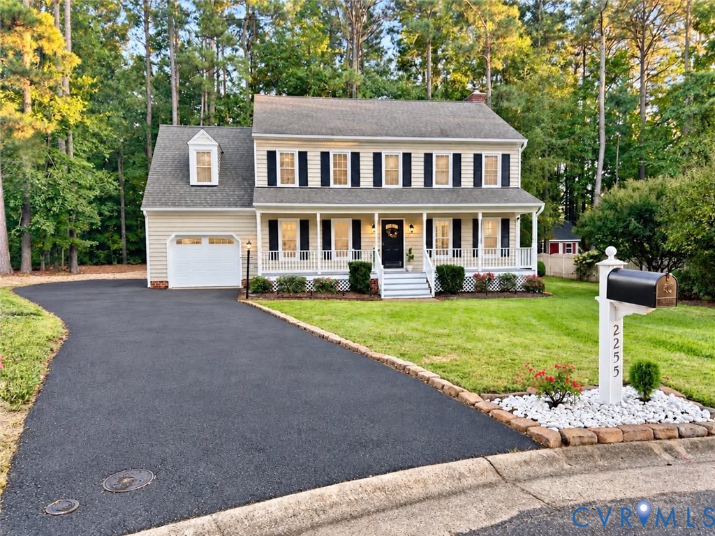 Two-story exterior featuring light-toned horizontal siding, a covered front porch with railing, a paved driveway, and established tree-lined landscaping