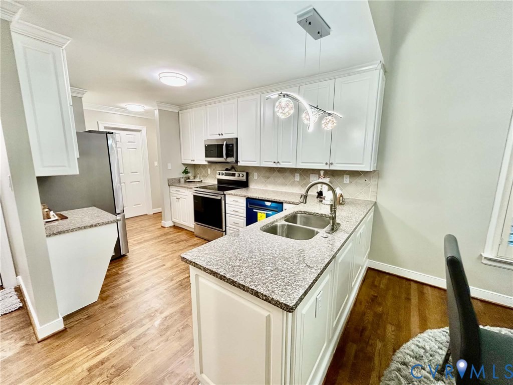 Kitchen featuring white shaker-style cabinetry, stone-finish countertops, stainless steel dual-basin sink, wood-finish flooring, and crown molding