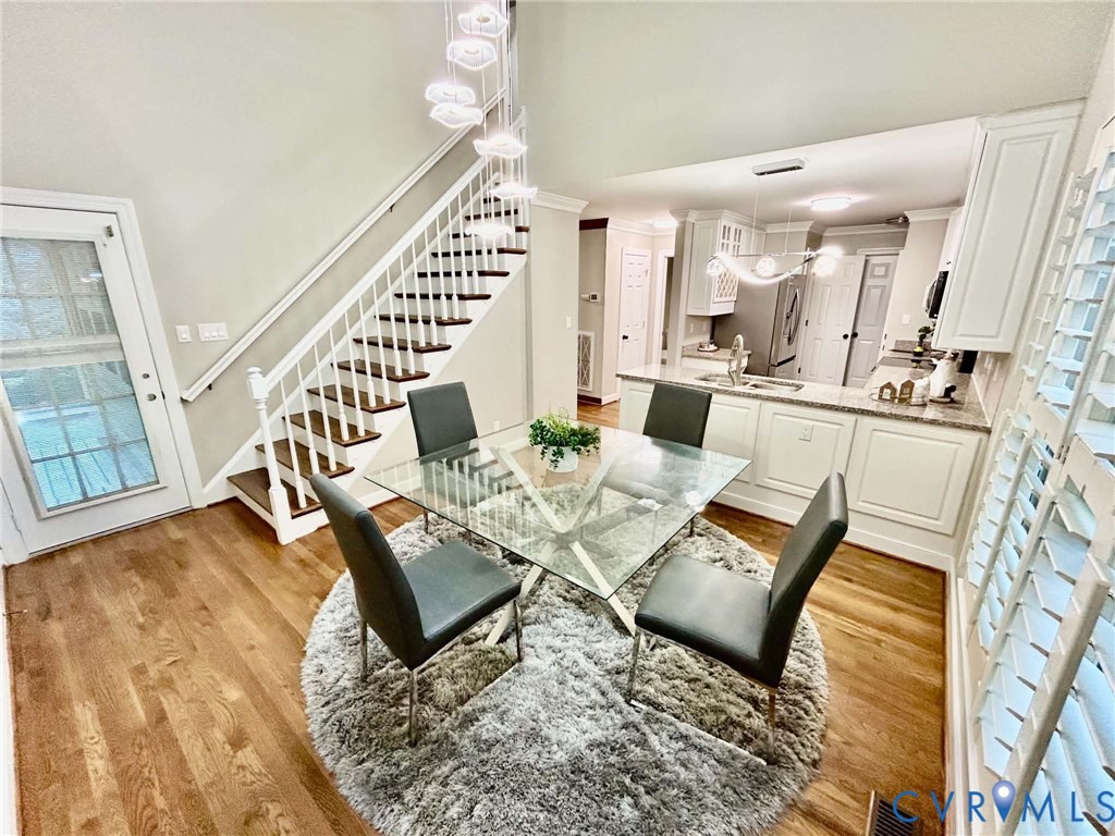 Open-concept floor plan with wood-finish flooring, vaulted ceilings, a staircase with white-finish banisters, built-in kitchen cabinetry, and multi-tier pendant lighting