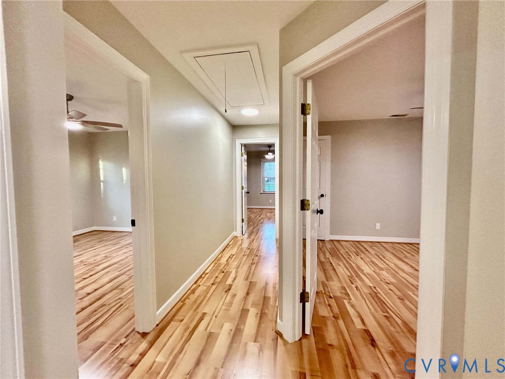 Interior hallway featuring wood-finish flooring, neutral wall paint, and multiple white-paneled interior doors