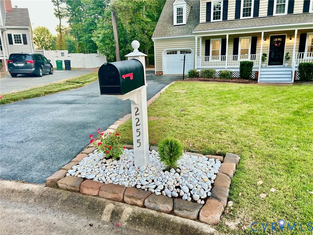 Colonial-style exterior featuring a covered front porch, asphalt driveway, and a decorative mailbox island with stone hardscaping