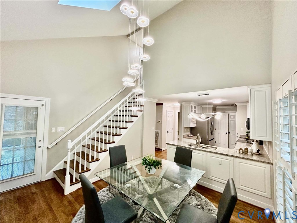 Vaulted ceiling featuring a tiered multi-light pendant fixture, wood-finish flooring, and a staircase with white painted balusters and wood-finish treads
