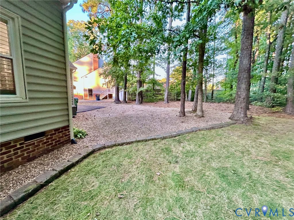 Exterior features include horizontal siding, a brick foundation, gravel ground cover, and mature trees