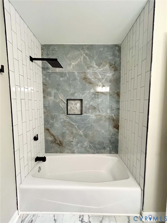 Alcove bathtub featuring white subway tile side walls, a large-format veined accent wall, a built-in recessed niche, and matte black plumbing fixtures