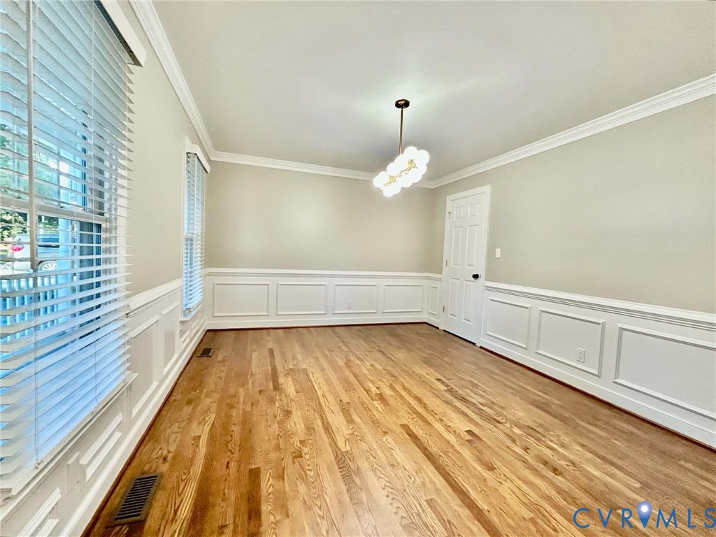 Interior space featuring wood-finish flooring, white wainscoting, crown molding, and a multi-globe light fixture