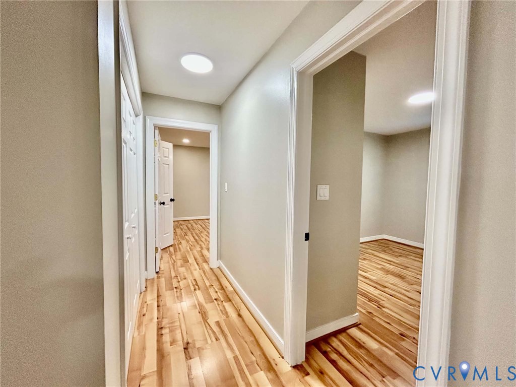 Hallway featuring wood-finish flooring, flush-mount ceiling lighting, and white door frames with matching panel doors