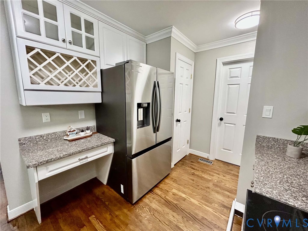 White cabinetry with glass-fronted upper doors, integrated wine rack, stone-finish countertops, stainless steel refrigerator, and wood-finish flooring