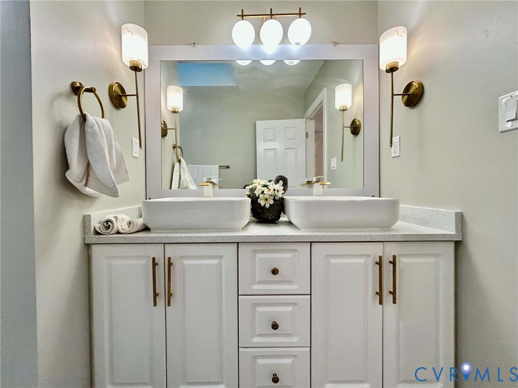 Double vanity featuring rectangular vessel sinks, quartz countertop, white cabinetry with metallic hardware, and integrated lighting fixtures