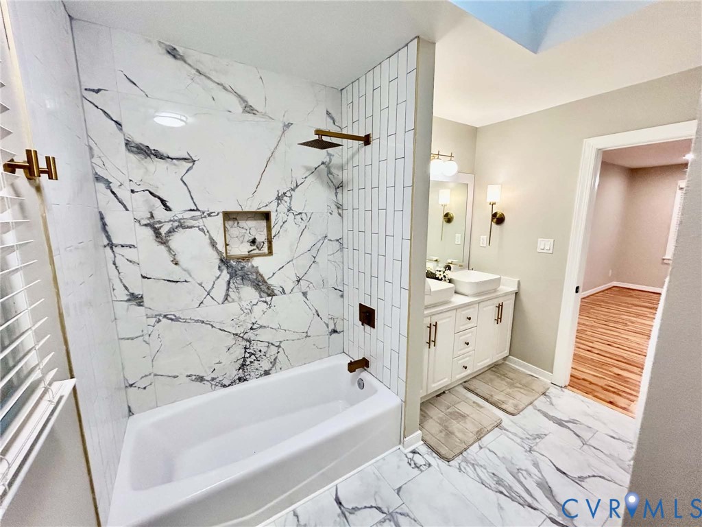 Bathroom featuring a tub-shower combination with floor-to-ceiling large-format veined tile, contrasting vertical subway tile surround, built-in recessed niche, and metallic bronze-tone fixtures, complemented by a white dual-sink vanity and matching veined floor tile