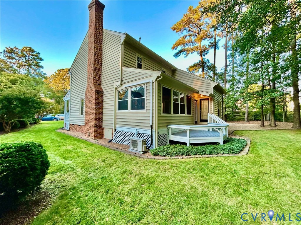 Exterior featuring light-colored horizontal siding, a full-height brick chimney, an elevated wooden deck, and manicured landscaping