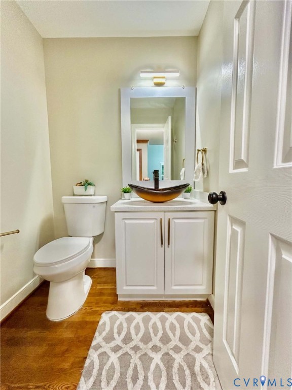 White vanity with a glass vessel sink, stone countertop, matte black faucet, and wood-finish flooring