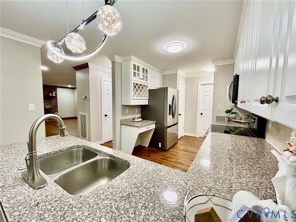 Kitchen featuring speckled stone countertops, dual-basin stainless steel sink with arch faucet, white cabinetry with built-in wine rack, wood-finish flooring, and contemporary multi-pendant lighting