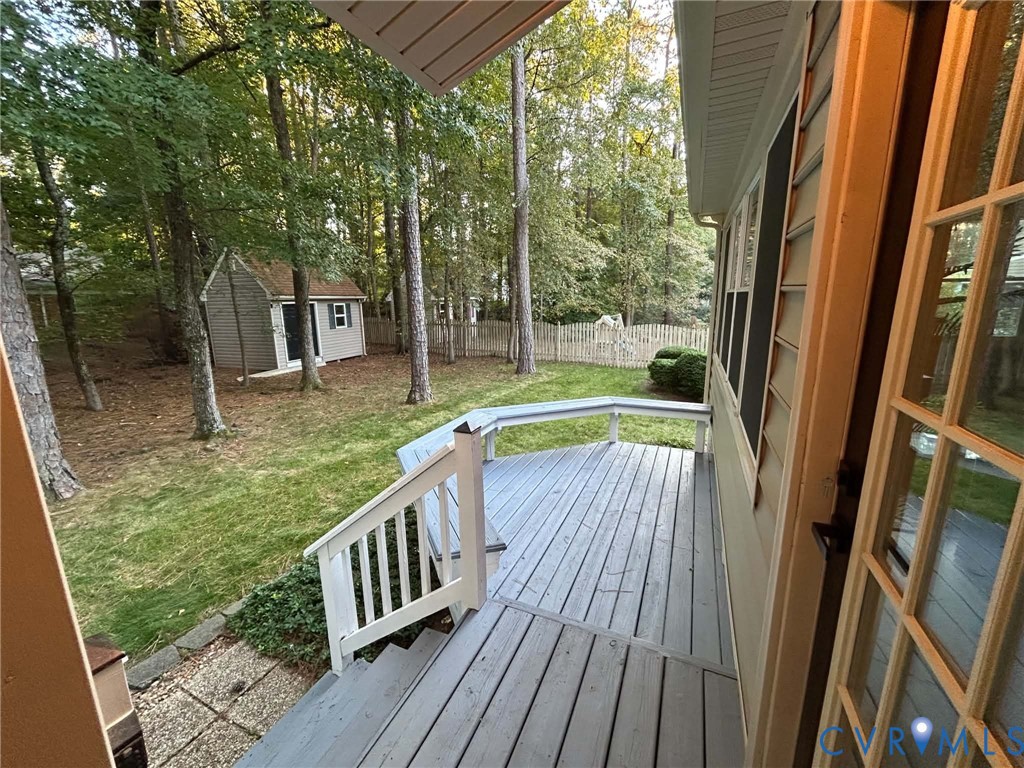 Elevated wood-plank deck featuring built-in bench seating, white railing, mature trees, and an exterior storage structure