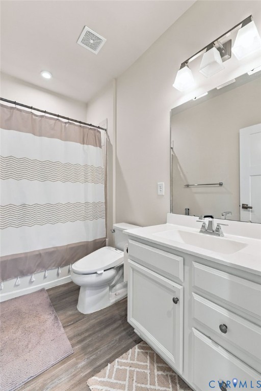 Bathroom featuring a white vanity with integrated basin, multi-light fixture, large wall mirror, wood-finish flooring, and a tub-shower combination