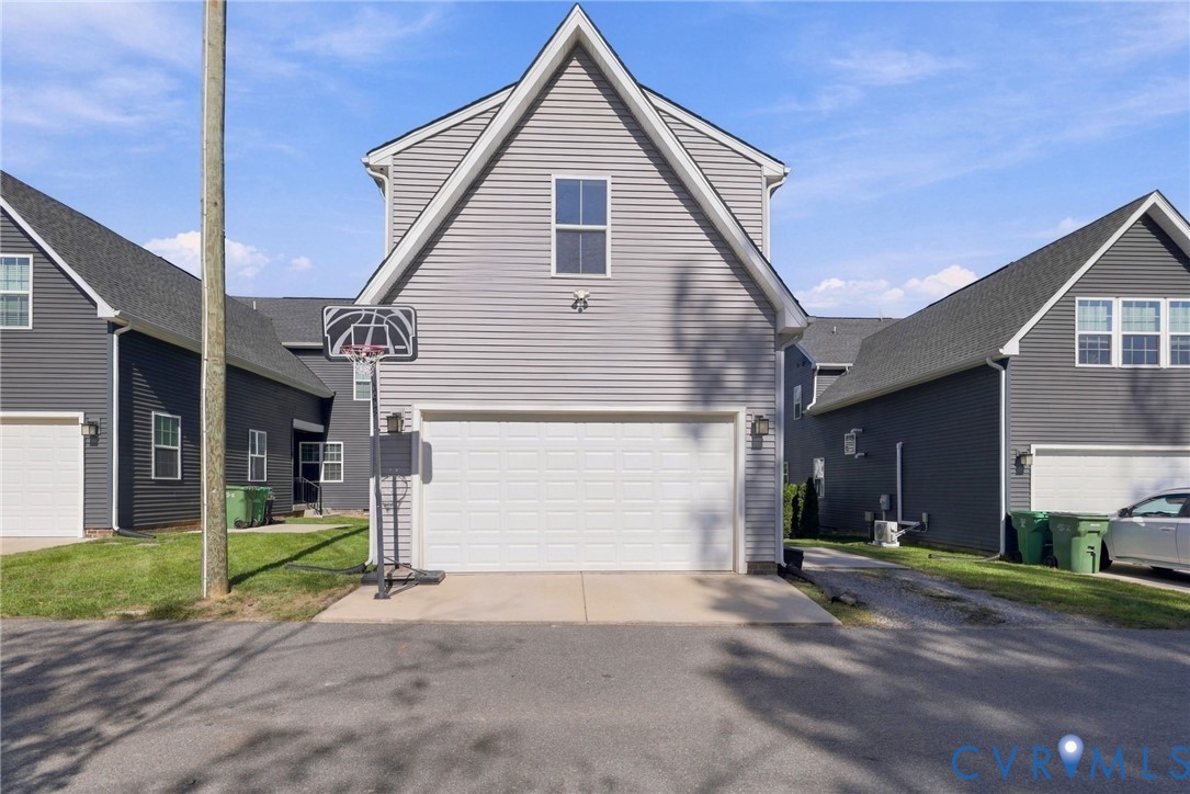 Two-story exterior featuring light gray horizontal siding, a gabled roofline, concrete driveway, and white sectional garage door