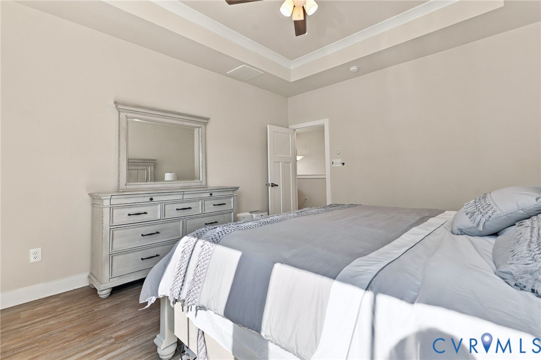 Tray ceiling with center-mount fan, wood-finish flooring, and multi-panel interior door