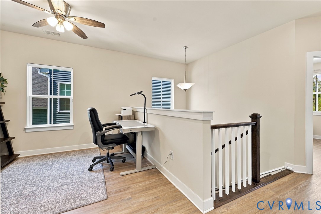 Wood-finish flooring, half-wall partition with a wooden cap, painted wood balusters with a dark wood newel post, multi-light ceiling fan, and pendant lighting