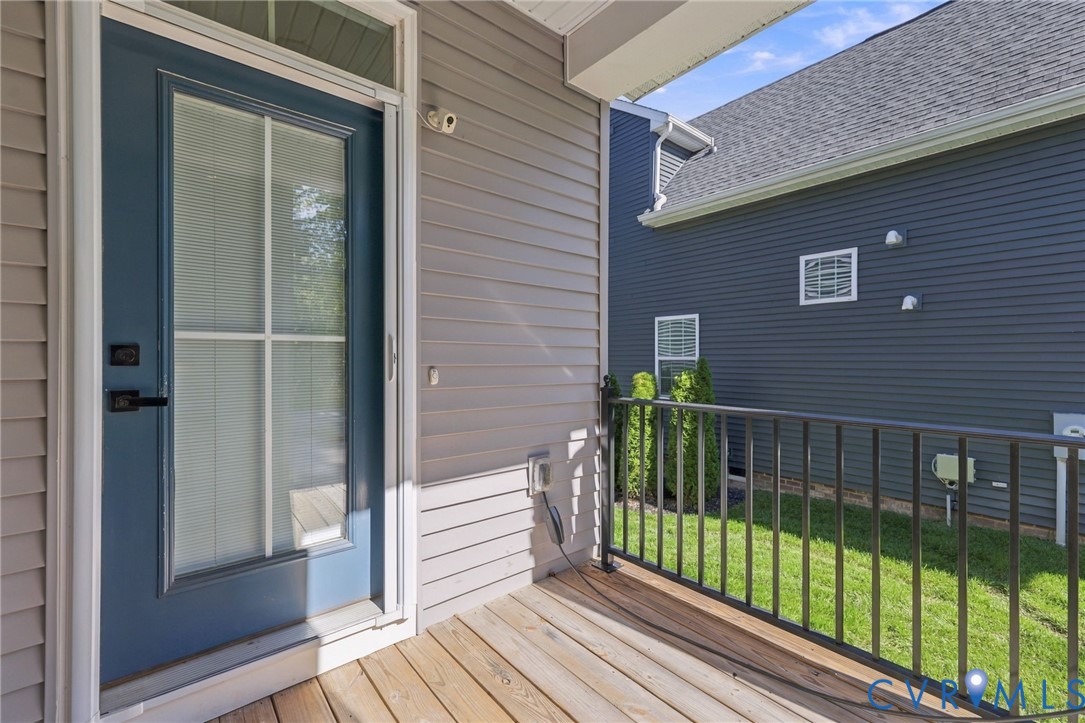 Covered porch featuring wood-plank decking, metal railing, and a blue exterior door with a glass-paneled storm door