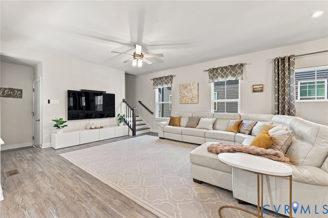 Living area featuring wood-finish flooring, recessed lighting, a multi-blade ceiling fan with integrated light, and windows with top-mounted treatments