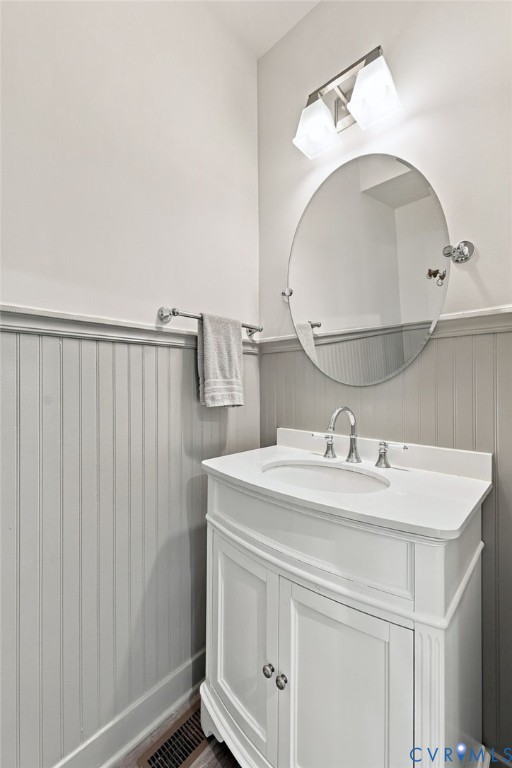 White vanity with integrated basin and polished chrome faucet, oval wall-mounted mirror, two-light fixture, and vertical beadboard wainscoting White vanity with integrated basin and polished chrome faucet, oval wall-mounted mirror, two-light fixture, and vertical beadboard wainscoting