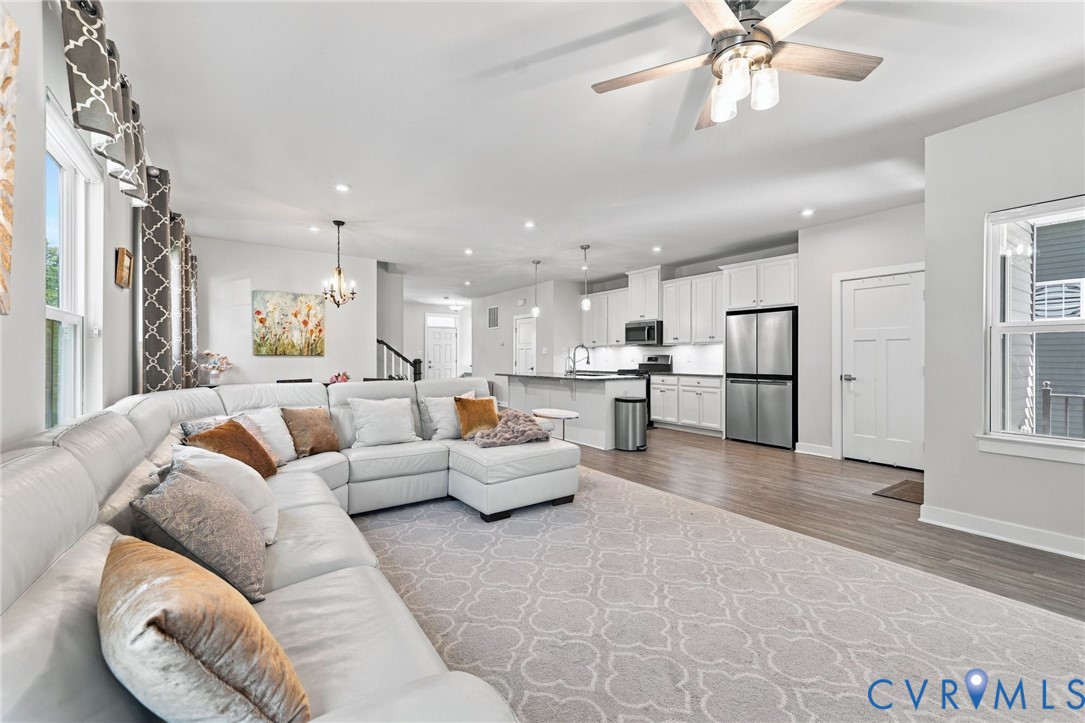 Open-concept living space featuring wood-finish flooring, white cabinetry, stainless steel appliances, recessed lighting, and a ceiling fan