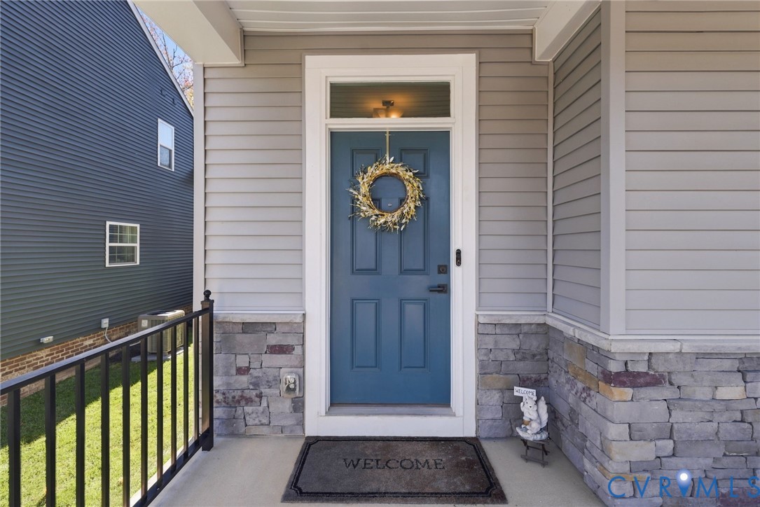 Covered entryway featuring a solid-panel blue door with a transom window, horizontal lap siding, and stone veneer base Covered entryway featuring a solid-panel blue door with a transom window, horizontal lap siding, and stone veneer base