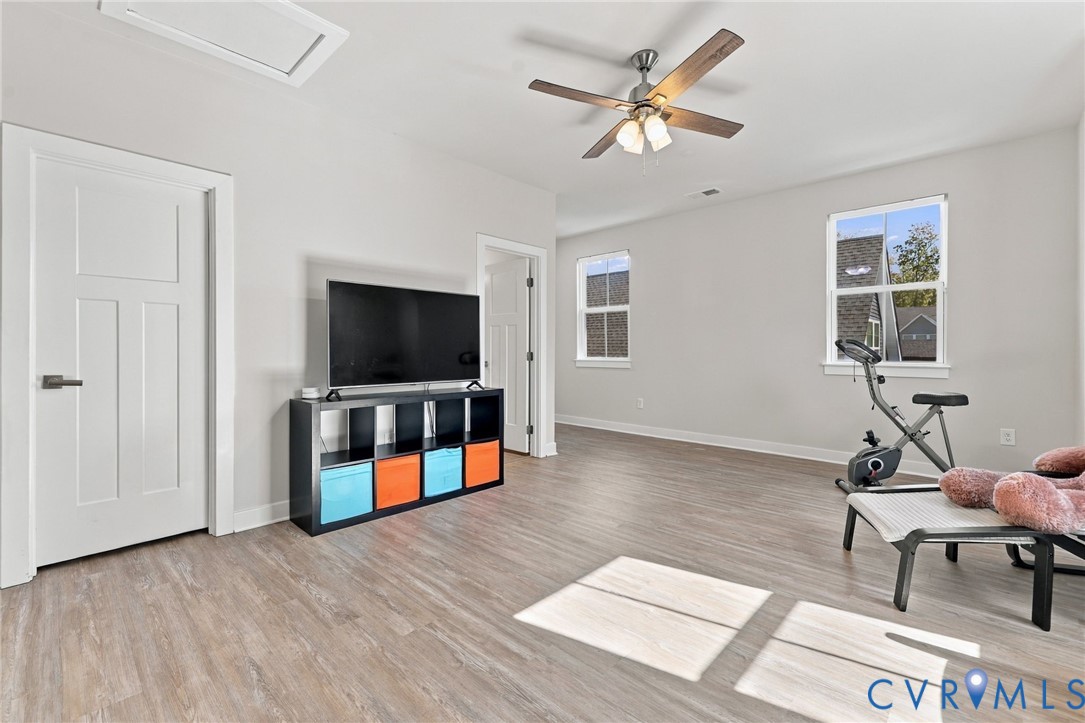 Neutral-toned room featuring wood-finish flooring, a ceiling fan with integrated lighting, and multi-pane windows