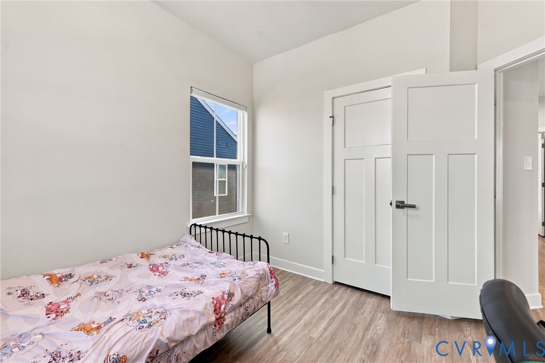 Room featuring wood-finish flooring, a single-hung window, and a three-panel shaker-style door with matte black hardware